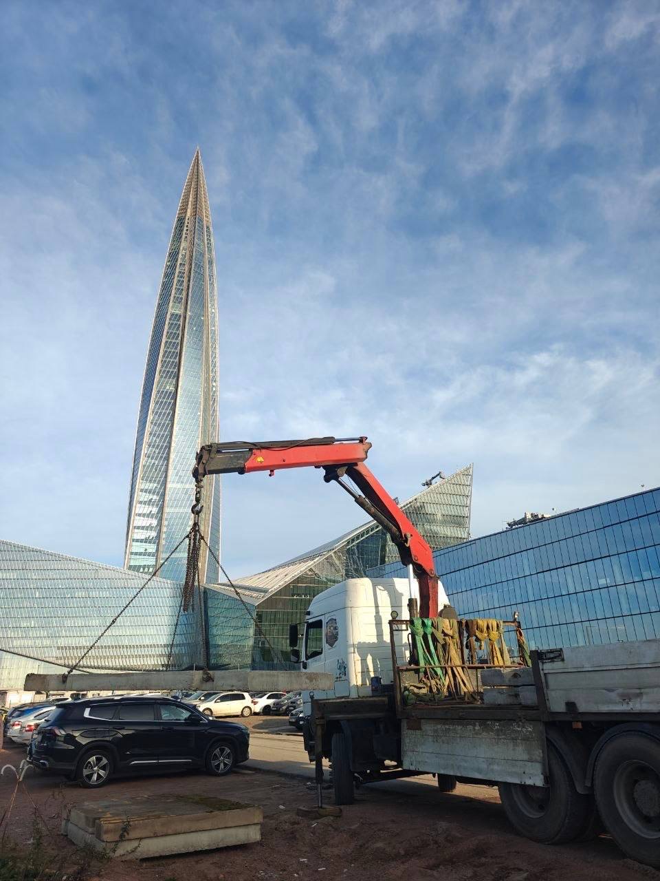 Манипулятор поднимает бетонный элемент на городской площадке
